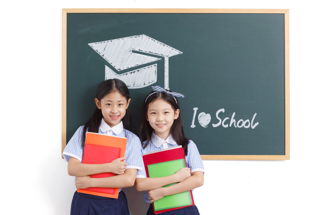 Crafting Captivating Headlines: Your awesome post title goes here Two cheerful schoolgirls holding notebooks, standing by a chalkboard in a classroom.