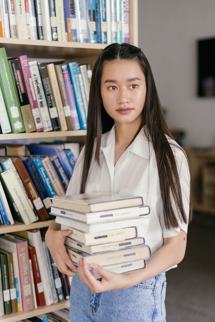 The Art of Drawing Readers In: Your attractive post title goes here Asian student holding books in a library, surrounded by bookshelves, studying for college.